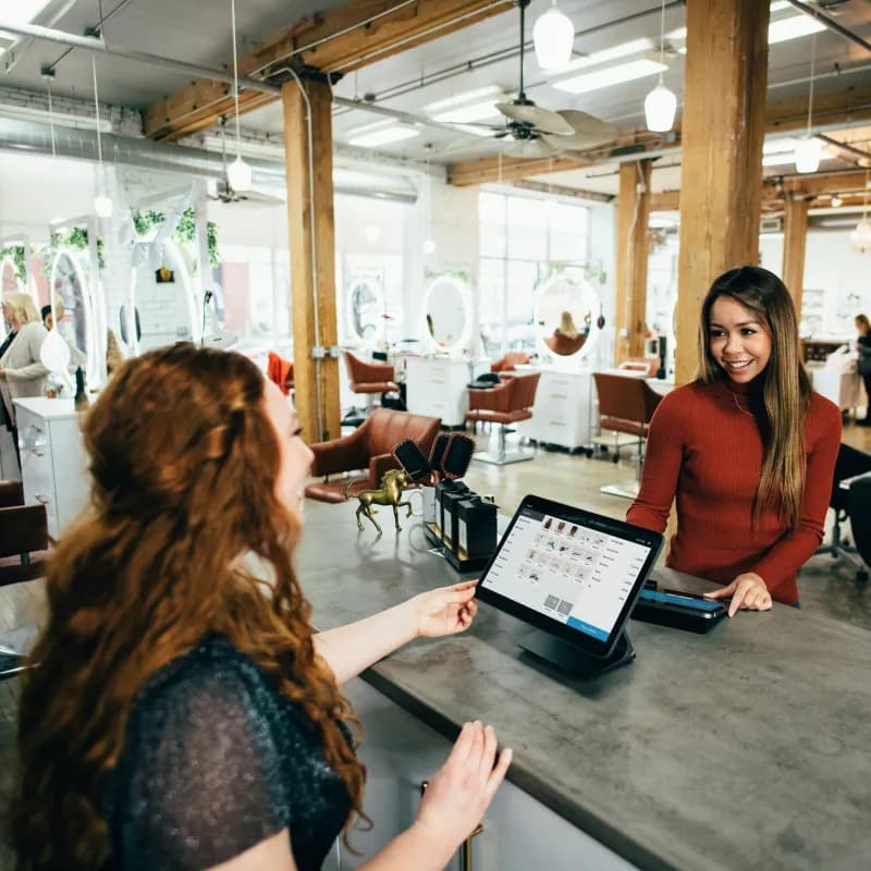 A salon owner taking a card payment from a client at the front desk